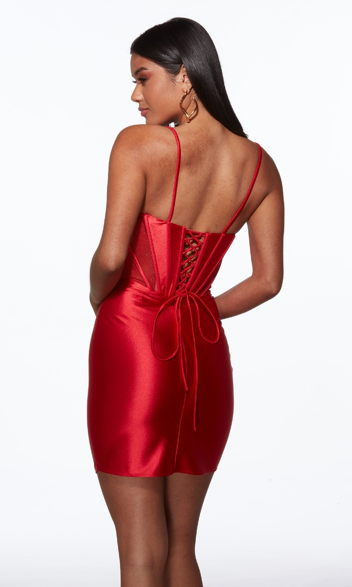 A woman models the Alyce 40117 Lace-Up Short Corset Hoco Dress, a red satin mini with spaghetti straps and lace-up back, posing with her back to the camera against a white background.